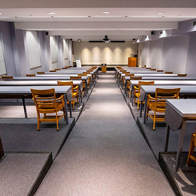 Tiered work tables in front of a presentation screen and podium.